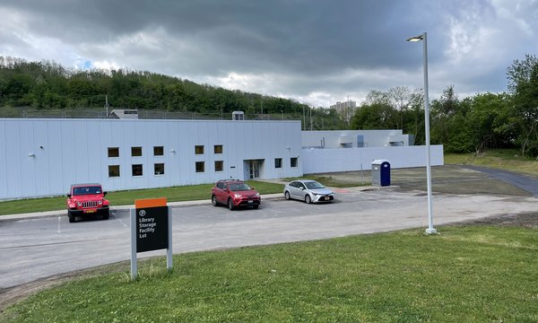 one story white building with cars and grass in front, gray clouds overhead