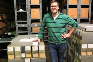 Dane Flansburgh standing next to archival boxes in a warehouse