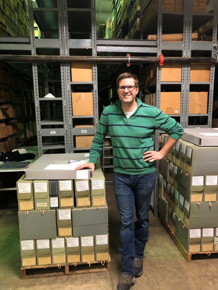 Dane Flansburgh standing next to archival boxes in a warehouse