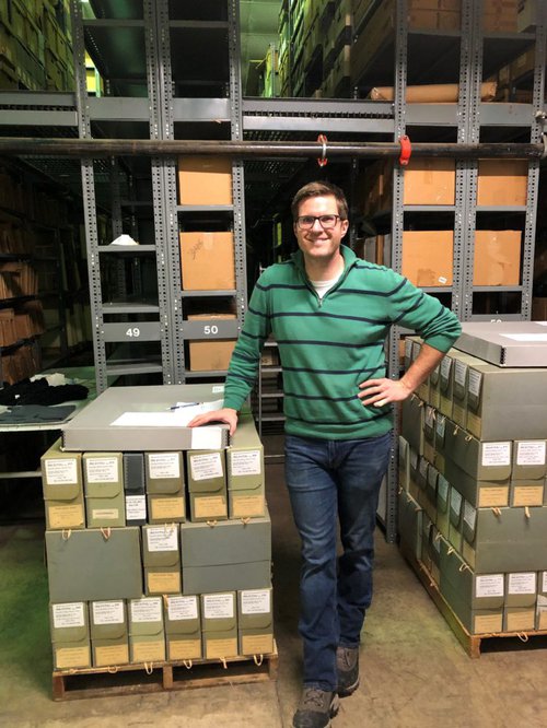 Dane Flansburgh standing next to archival boxes in a warehouse.