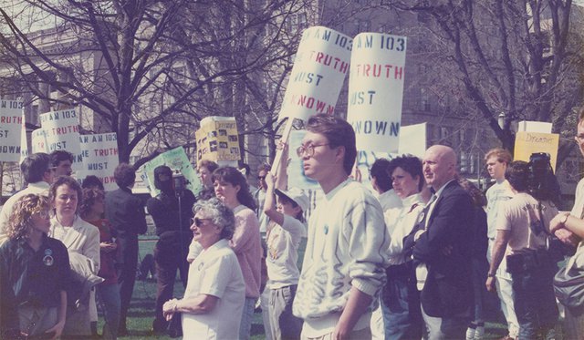 Archival photo of group gathered holding signs that read "Pan Am 103 The Truth Must Be Known"