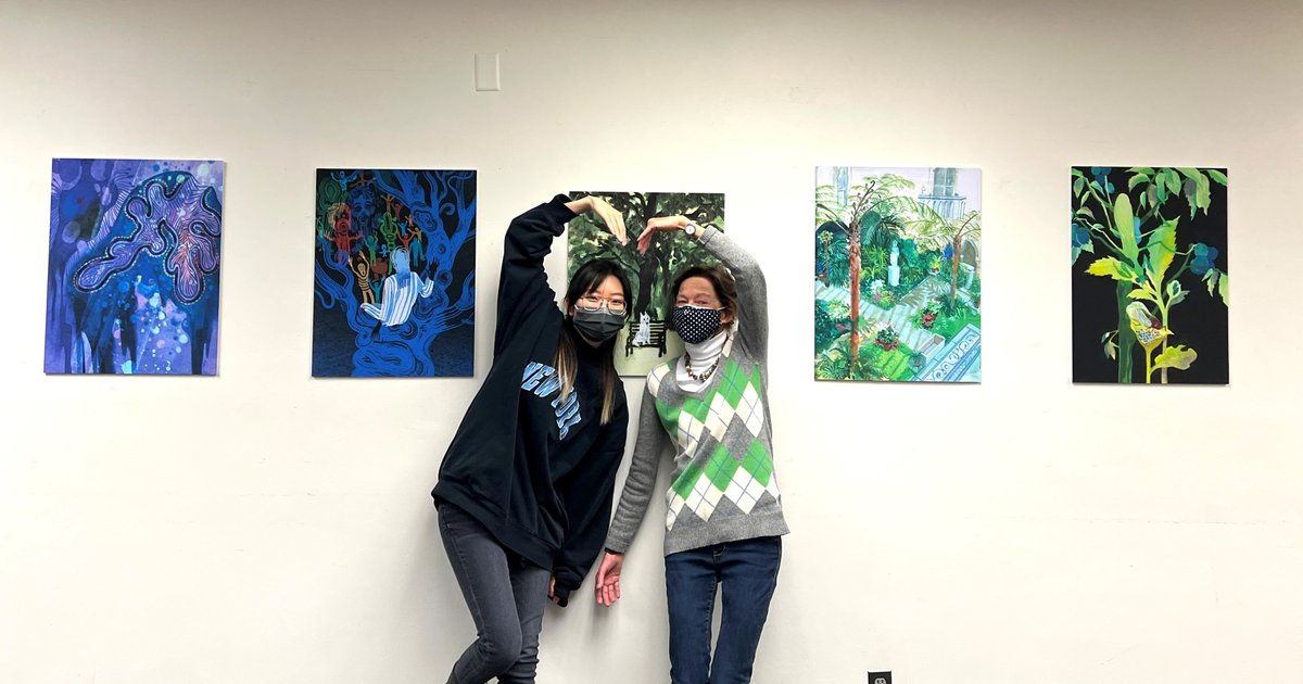 Artist Xuan Liu and Librarian S. Ann Skiold posing in front of  abstract artwork and making a heart with their arms