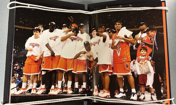 The Syracuse University Men’s Basketball team just after their 2003 NCAA Championship win. They wear shirts that read “National Champions” and are celebrating together. Carmelo Anthony is third from the left in the front row.