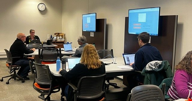 people working at tables with monitor/screen at each table