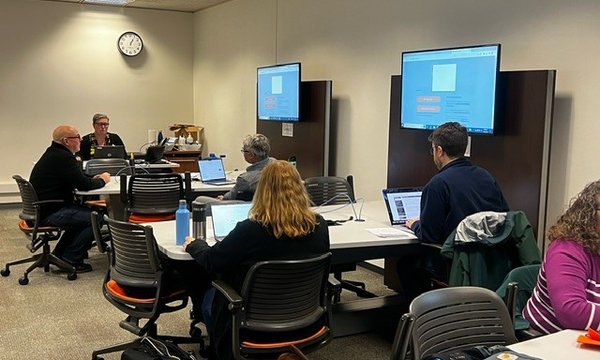 people working at tables with monitor/screen at each table
