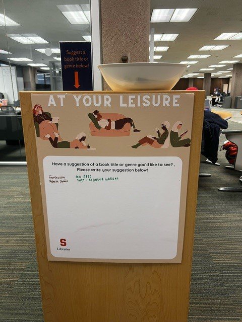 poster that says "At Your Leisure" and has space to write book title suggestions