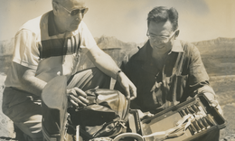 Sepia toned photo of two men looking at supplies in a backpack