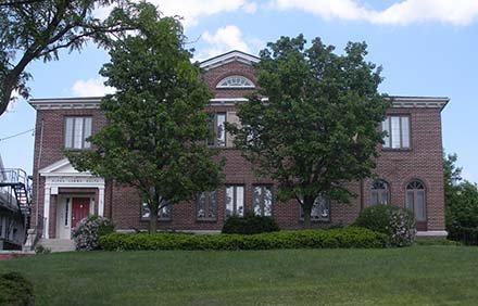 stately brick colonial house with door on left side, trees and grass in front