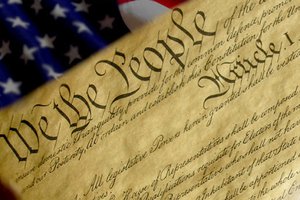 constitution document that reads "We the people..." and American flag behind it