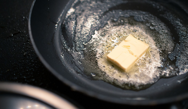 Close up of a pad of butter heating and melted in a black pan