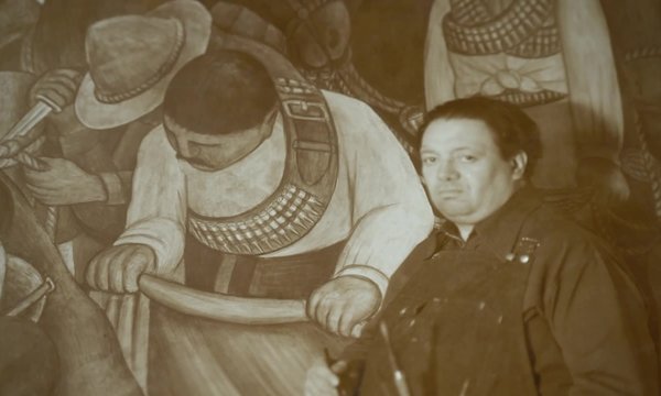 black and white of male artist on left in front of blown-up painting behind him