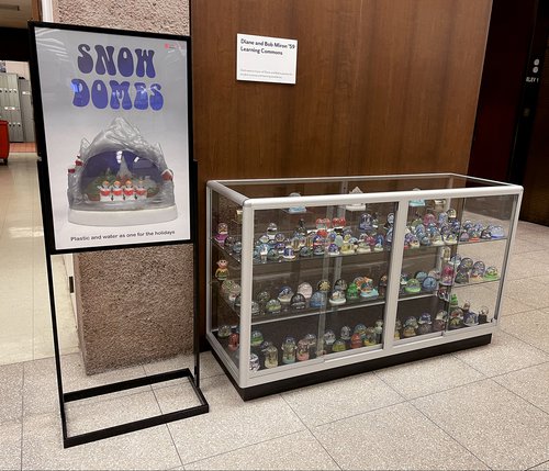 display with Snow Domes poster on left side next to glass case holding mini snow globes