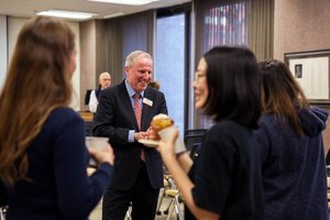 man in suit amid group of students eating donuts