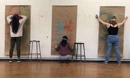 three students each standing in front of brown craft paper on wall in different poses