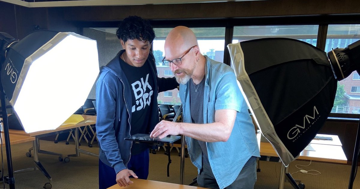 student and professor standing next to table with lighting on side to photograph item on table