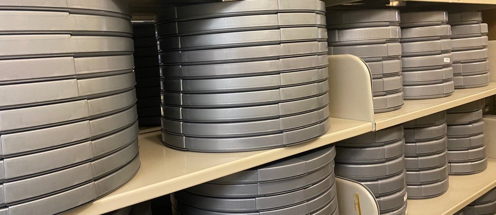 Rows of circular gray film cans stacked on shelves