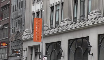 ornate gray concrete building with orange flag in front that reads "Fisher Center"