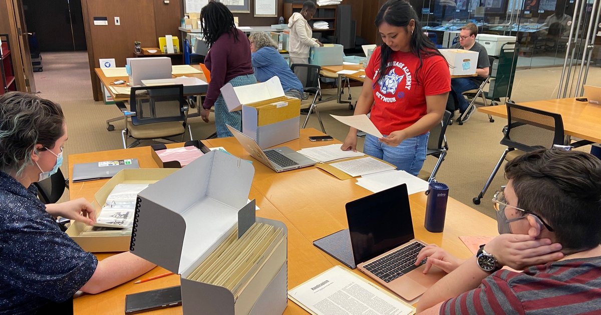 people sitting and standing at tables with files and papers in front of them