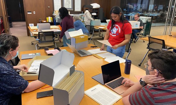 people sitting and standing at tables with files and papers in front of them