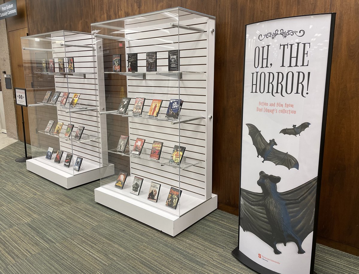 2 display cases with videos next to a poster that says "Oh, the Horror!" with flying bats