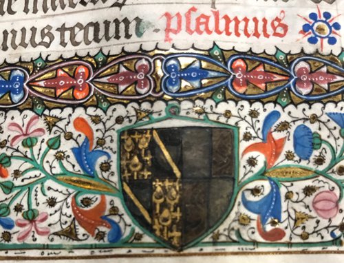 Close-up detail of a black and gold family crest with red, orange, pink, green, blue, and gold floral designs below red and black Latin text on vellum.