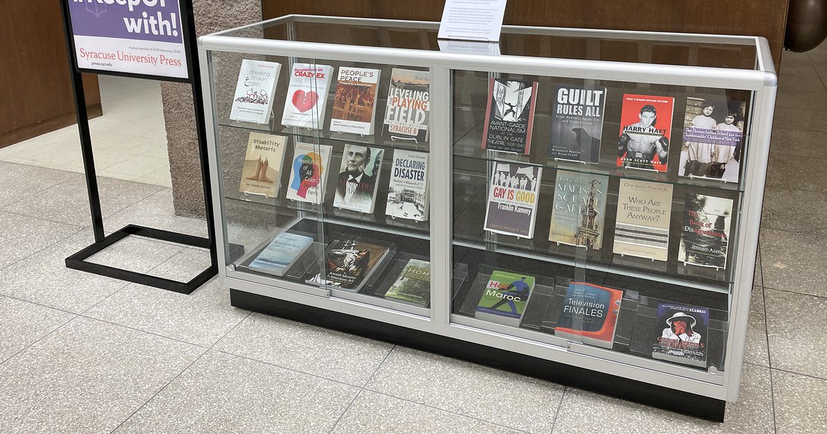 University Press Week display with purple poster and rows of books in a glass display case
