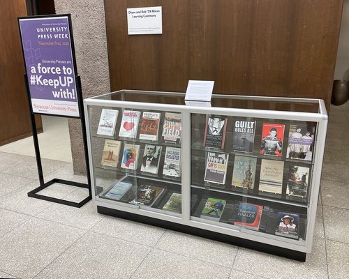 poster with words "University Press Week; a force to #KeepUP with!" next to glass display case featuring books
