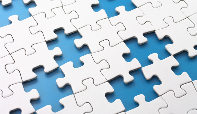 Close up of white puzzle pieces connected with several pieces missing in between, revealing a light blue background
