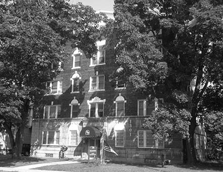 four story brick building with white exterior on first floor, view obstructed by trees