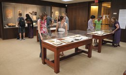 room with glass display cases along walls and glass display tables on floor. people looking at materials on display