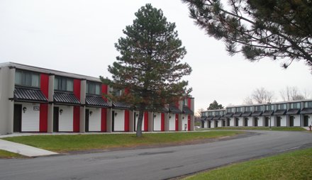 concrete building designed like motel with individual entrances for each unit, red trim overhang over each door