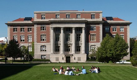 large Renaissance beaux-arts building with four columns in front, students sitting on grass in front of building