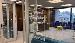 glass enclosed room with words Syracuse Office of Undergraduate Research and Creative Engagement printed on glass wall