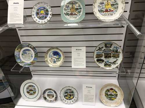 souvenir plates in display case with cards that read "Alaska" "Arizona" and "Arkansas"