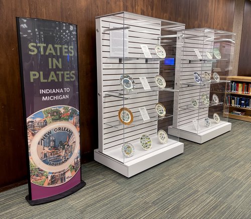 poster on left that reads "States in Plates, Indiana to Michigan" next to two glass display cases with plates and descriptions in each case