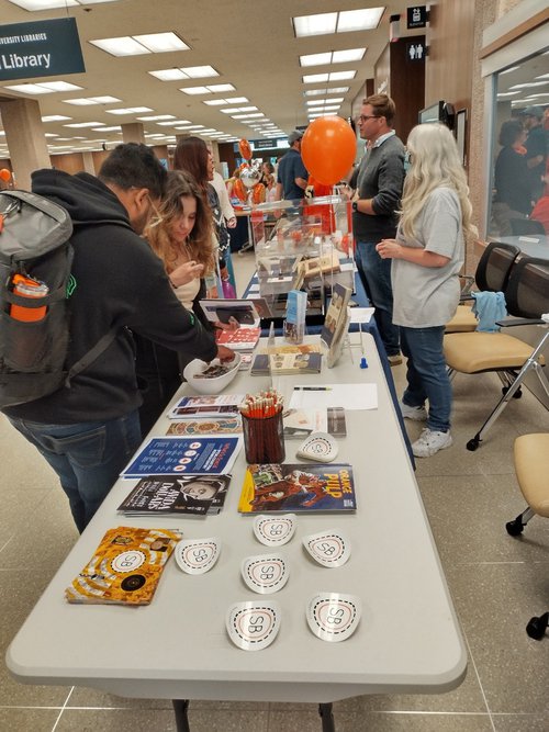 students dig for pins at table with handout materials in library