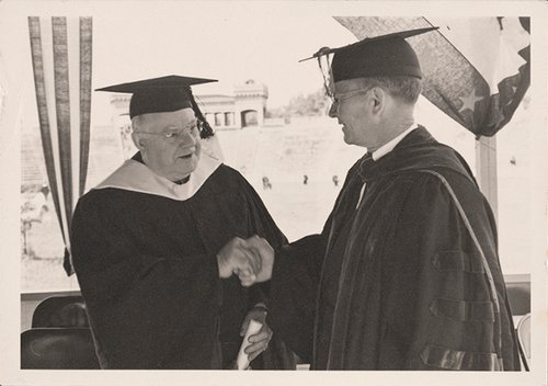 two men shaking hands, both wearing graduation cap and gown