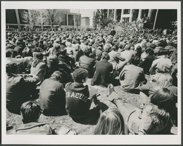 black and white photo of thousands of students sitting on grass facing Hendricks Chapel