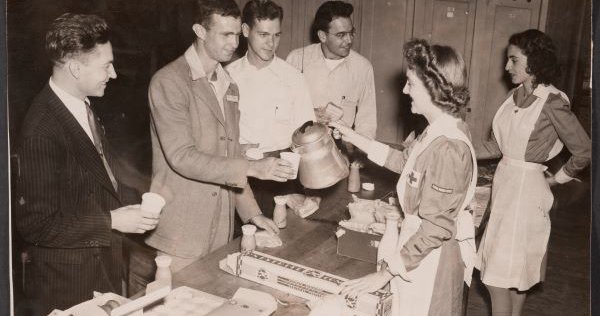 b&w male students lined up around table being served by female students