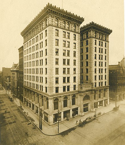 sepia photo of large multi story renaissance building that appears to be two twin towers with shorter building in center connecting them