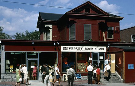 wood frame house converted to storefront with sign that says "university bookstore," people walking in and out of building