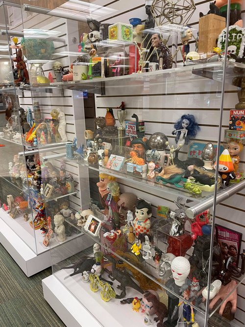 glass display case packed with various figurines, dolls, trinkets, toys, etc.